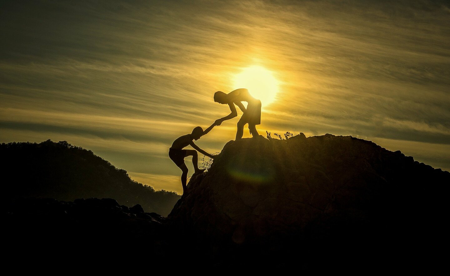 Boy holder the hand of another boy in order to help him reach the top of a mountain